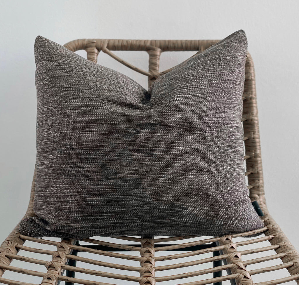 Textured gray pillow on a wicker chair against a plain background