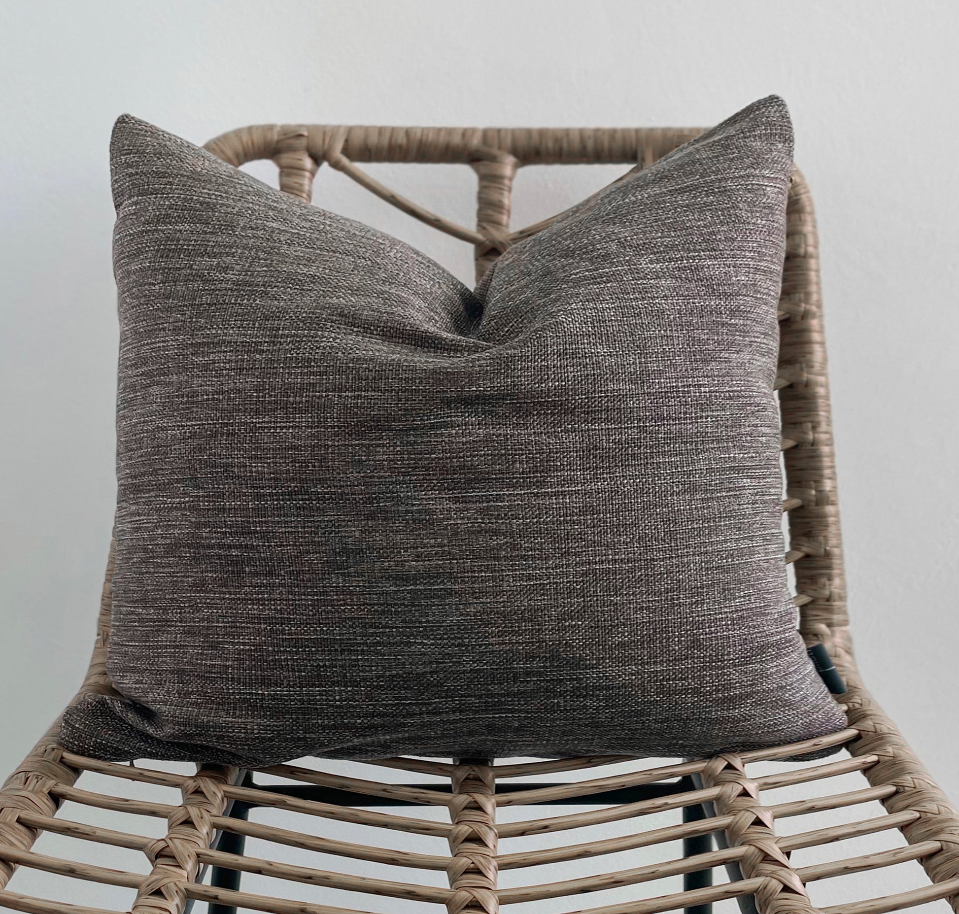 Textured gray pillow on a wicker chair against a plain background
