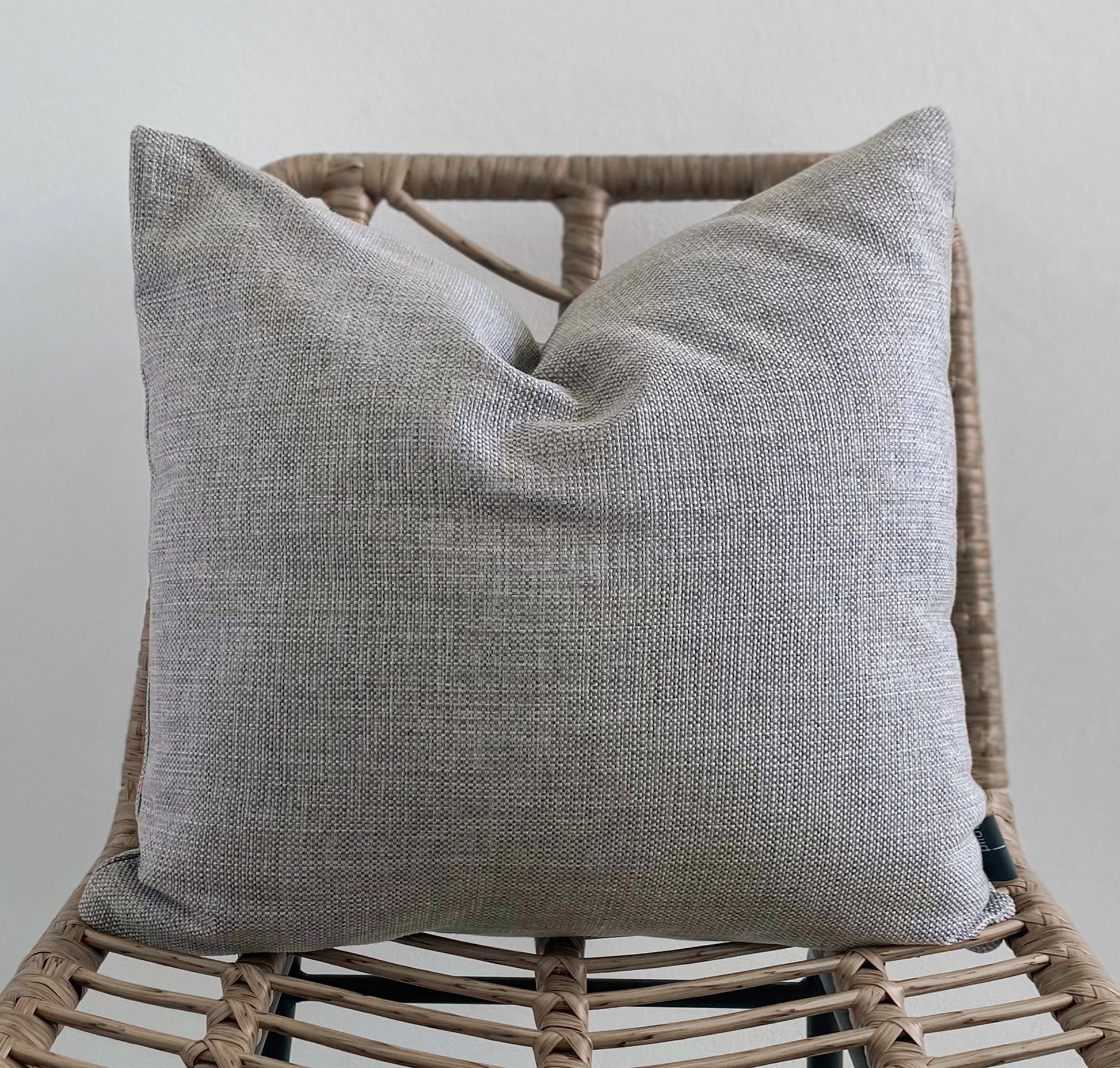 Gray textured pillow on a wicker chair against a light gray background