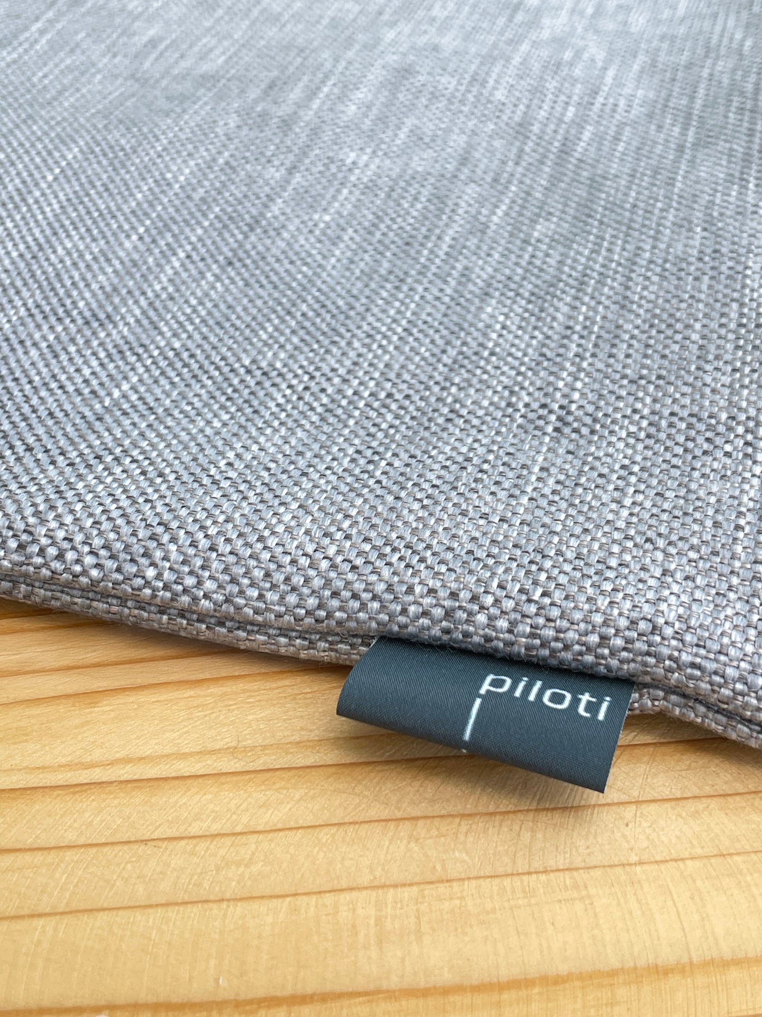 Gray fabric pillow with 'piliotti' label on a wooden surface