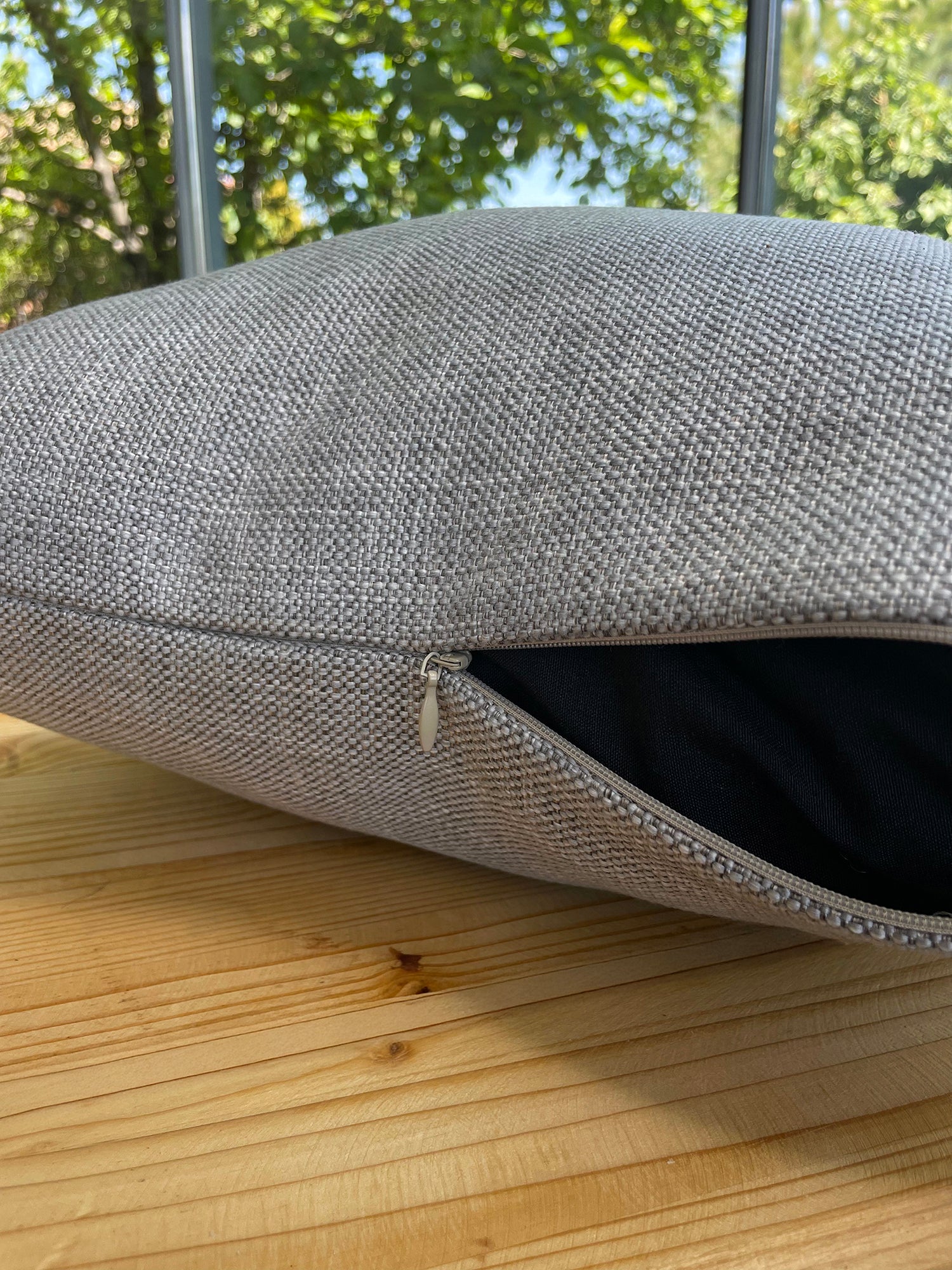 Gray textured cushion on a wooden surface with greenery in the background