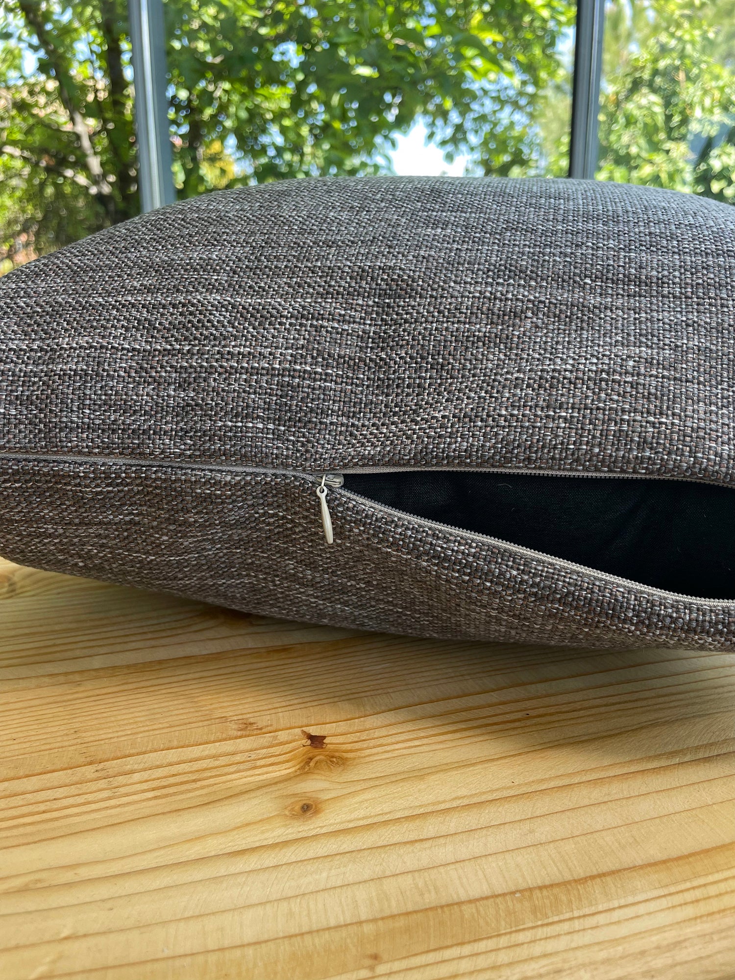 Gray textured cushion on a wooden surface with greenery in the background