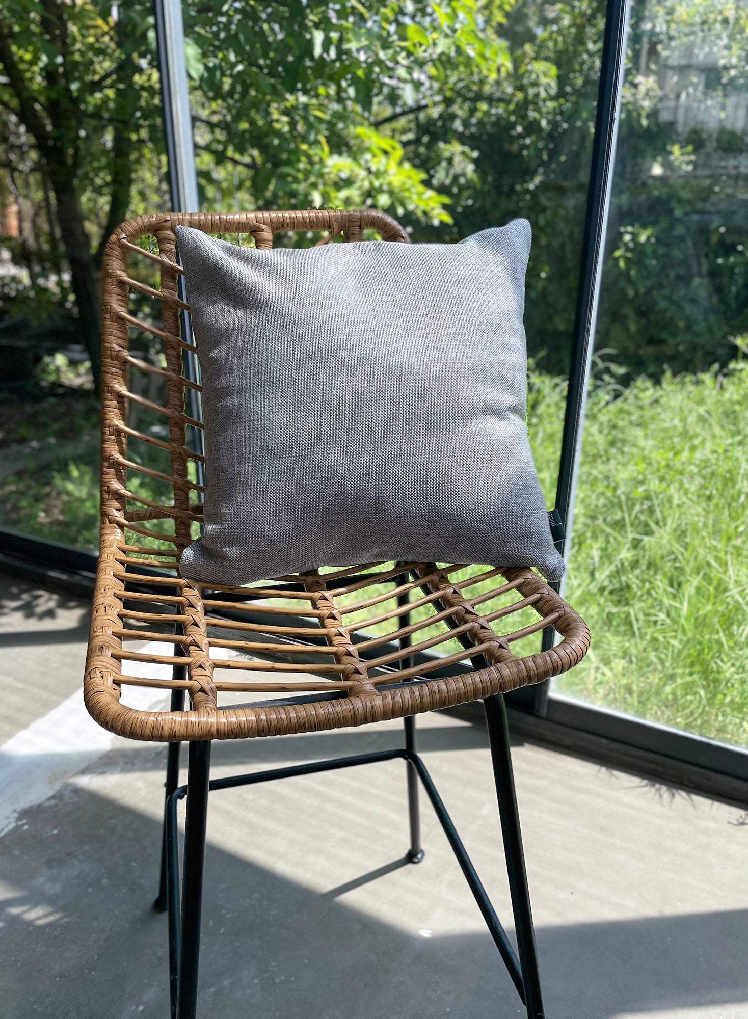 Wicker chair with a gray cushion on a patio with greenery outside