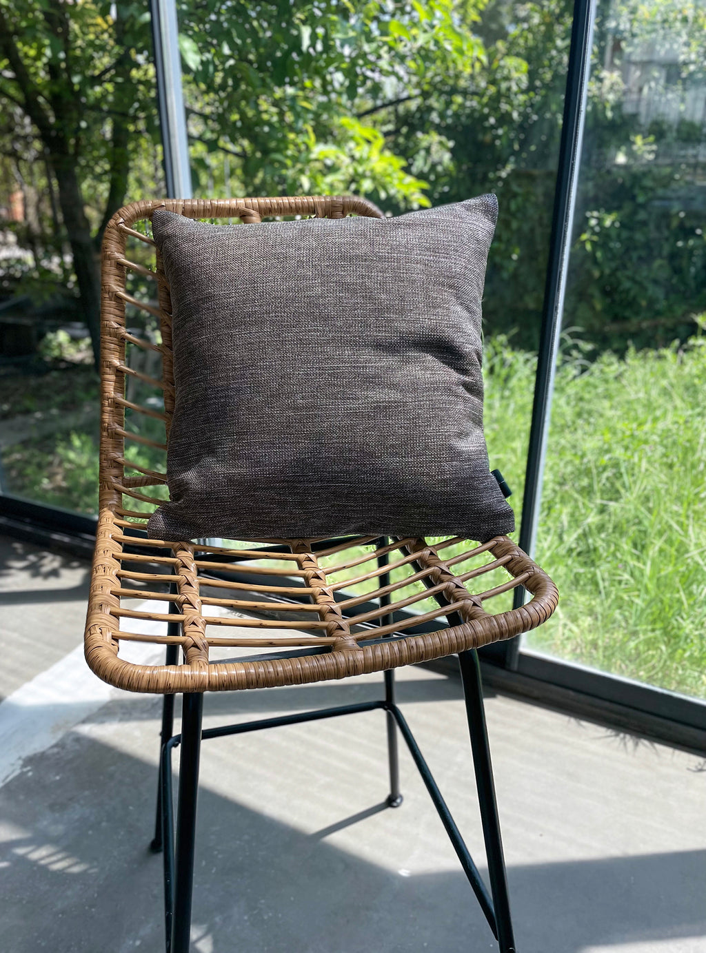 Wicker chair with a gray cushion on a patio with greenery in the background