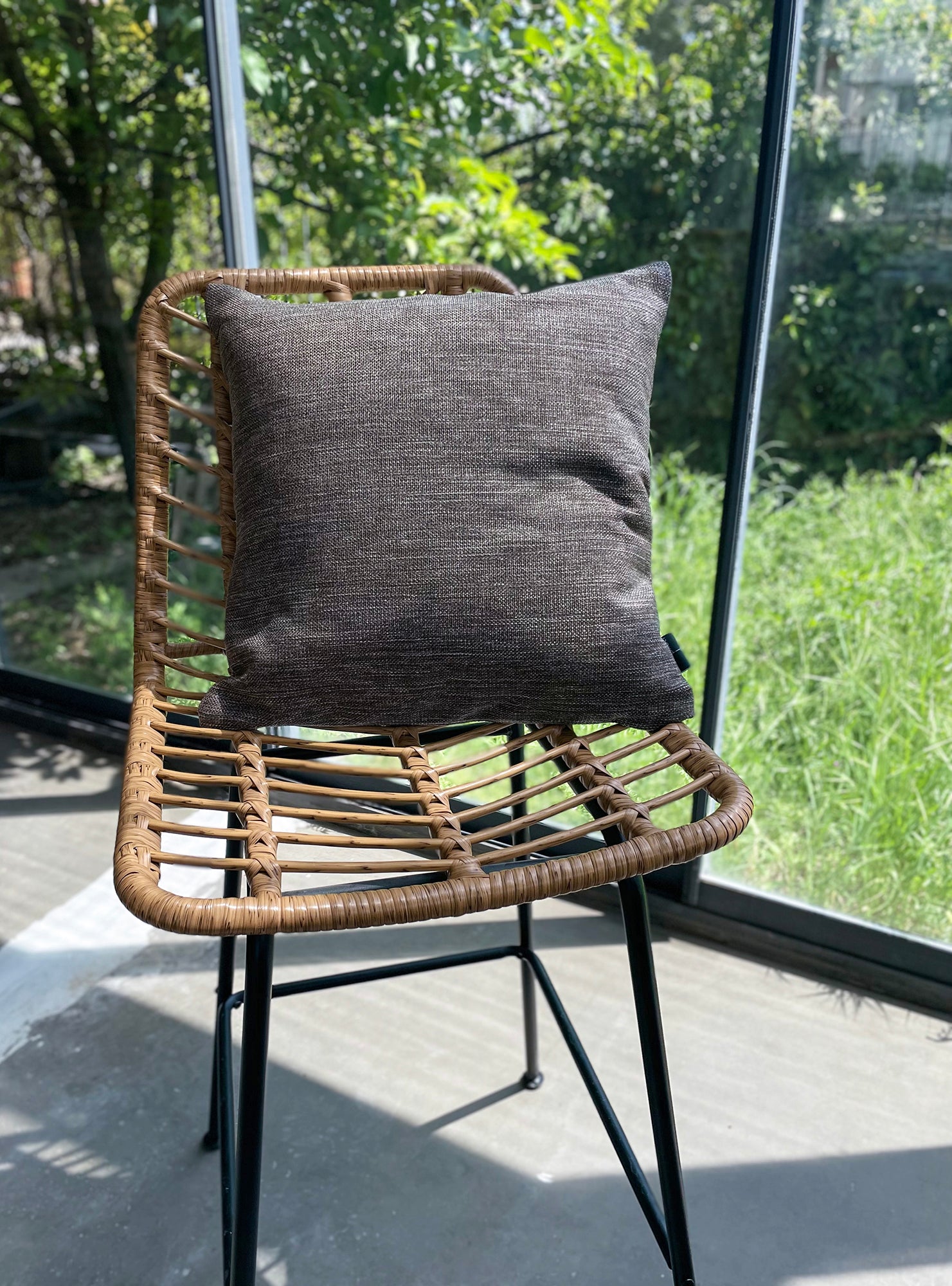 Wicker chair with a gray cushion on a patio with greenery in the background